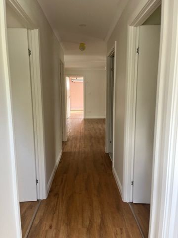 Hallway with wood floor, white walls and door frames. Two closed doors on either side, one open doorway at the end — Steel Homes Australia in Branyan, QLD