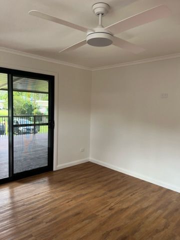 Empty room with wooden floor, white walls, ceiling fan, and sliding glass door leading to a deck — Steel Homes Australia in Branyan, QLD