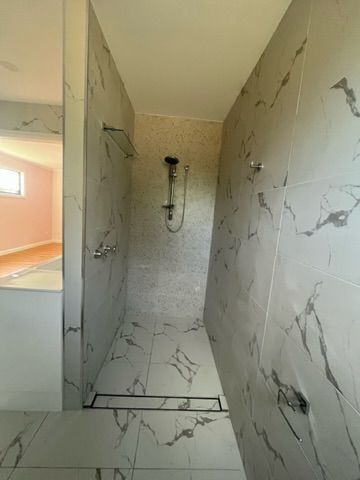 Bathroom with marble-like tiles, shower head, and a linear drain on the floor — Steel Homes Australia in Branyan, QLD