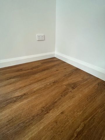 Brown wood-look flooring meets white walls and trim. Electrical outlet in the corner — Steel Homes Australia in Branyan, QLD