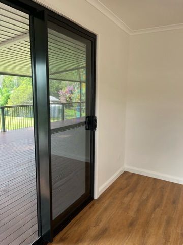 Sliding glass door with black frame leading to a wooden deck. Interior has white walls and wood flooring — Steel Homes Australia in Branyan, QLD