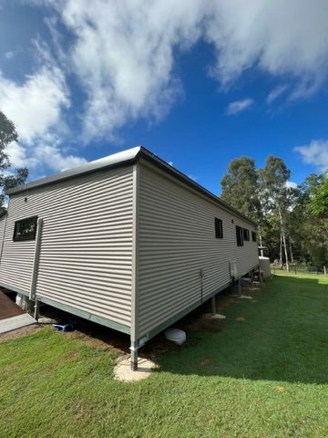 Beige corrugated metal-clad house on stilts against a blue sky with trees and green grass — Steel Homes Australia in Branyan, QLD