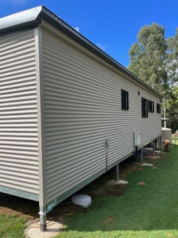 Beige corrugated metal building with black-framed windows, supported by stilts on a grassy lawn — Steel Homes Australia in Branyan, QLD