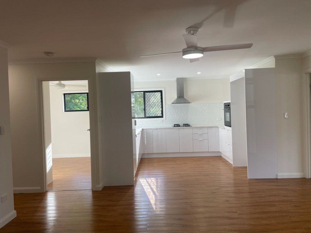 Bright kitchen with white cabinets, a stainless steel range hood, and wooden floors — Steel Homes Australia in Branyan, QLD