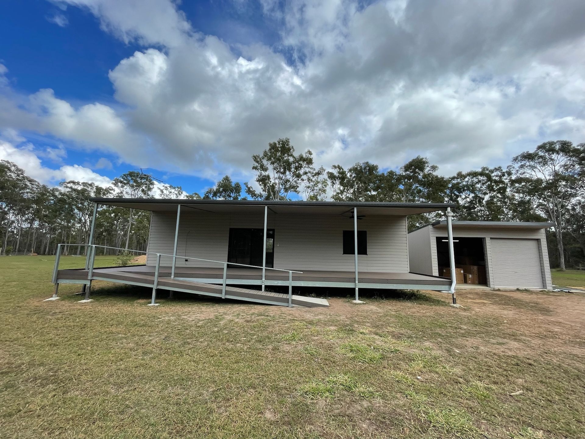 Ranch-style building with ramp in grassy field under cloudy sky. Shed to the right — Steel Homes Australia in Branyan, QLD