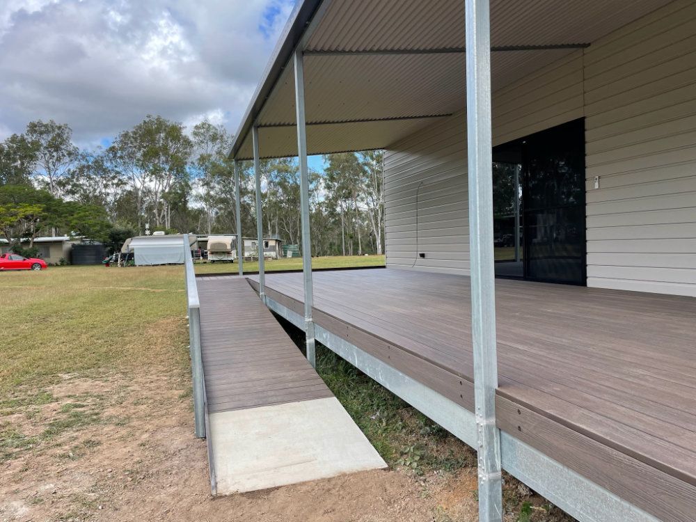 Ramp leading to a home with a deck. The home has white siding and a metal roof. Green grass and trees are in the background — Steel Homes Australia in Branyan, QLD