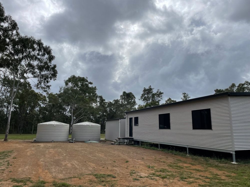 Gray modular home and water tanks on a dirt lot under a cloudy sky — Steel Homes Australia in Branyan, QLD