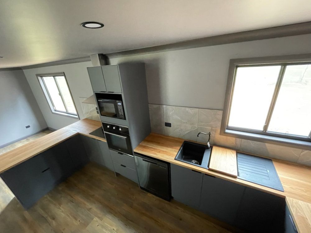 Modern kitchen with gray cabinets, wood counters, and stainless steel appliances — Steel Homes Australia in Branyan, QLD