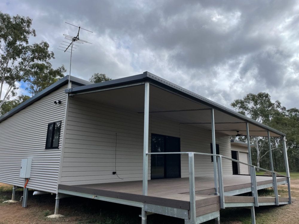 A beige house with a gray roof and a wooden deck under a cloudy sky. An antenna is on top — Steel Homes Australia in Branyan, QLD