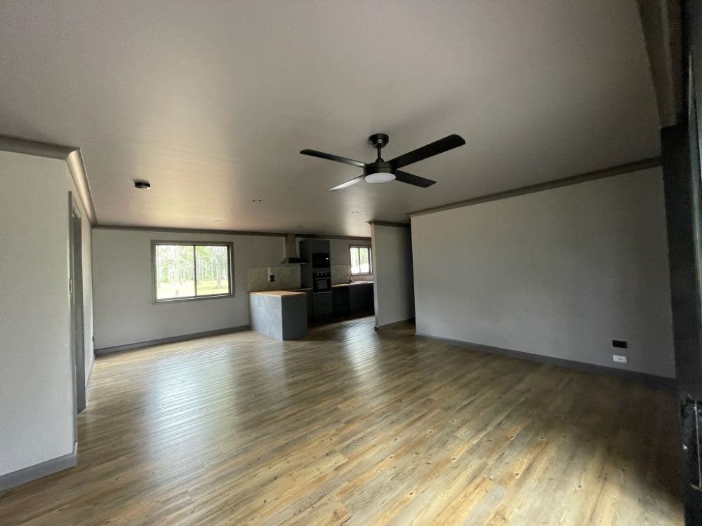 Interior of a living space with wooden floors, a grey ceiling, and a kitchen visible in the back — Steel Homes Australia in Branyan, QLD
