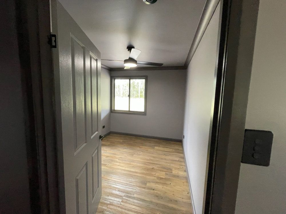 Open doorway to a bedroom with a window. Light wood floors, gray walls, and ceiling fan — Steel Homes Australia in Branyan, QLD