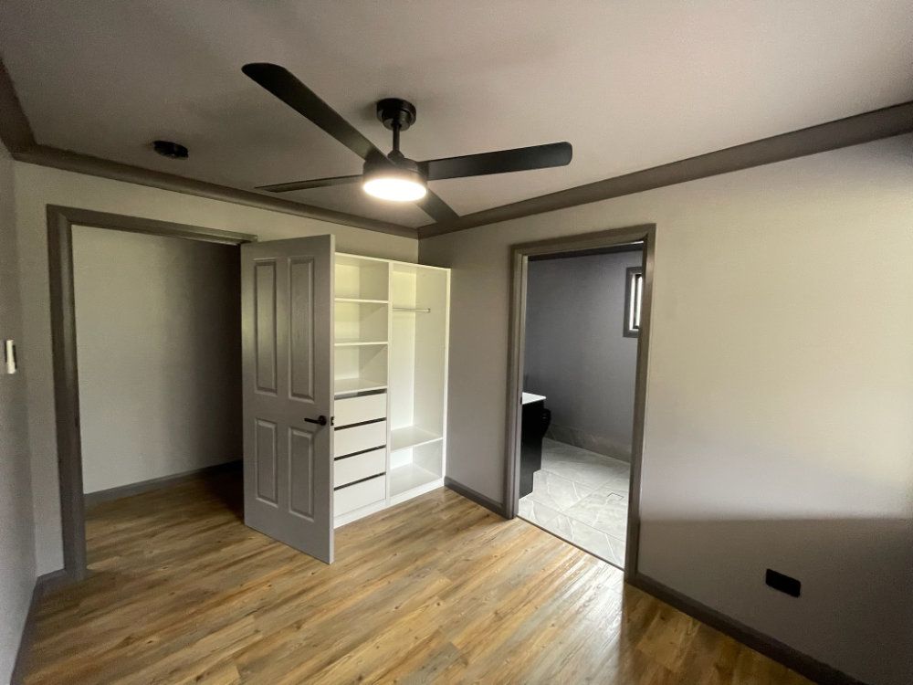 Empty bedroom with wood floor, white closet, and doorway to a bathroom. Dark gray trim, gray walls — Steel Homes Australia in Branyan, QLD