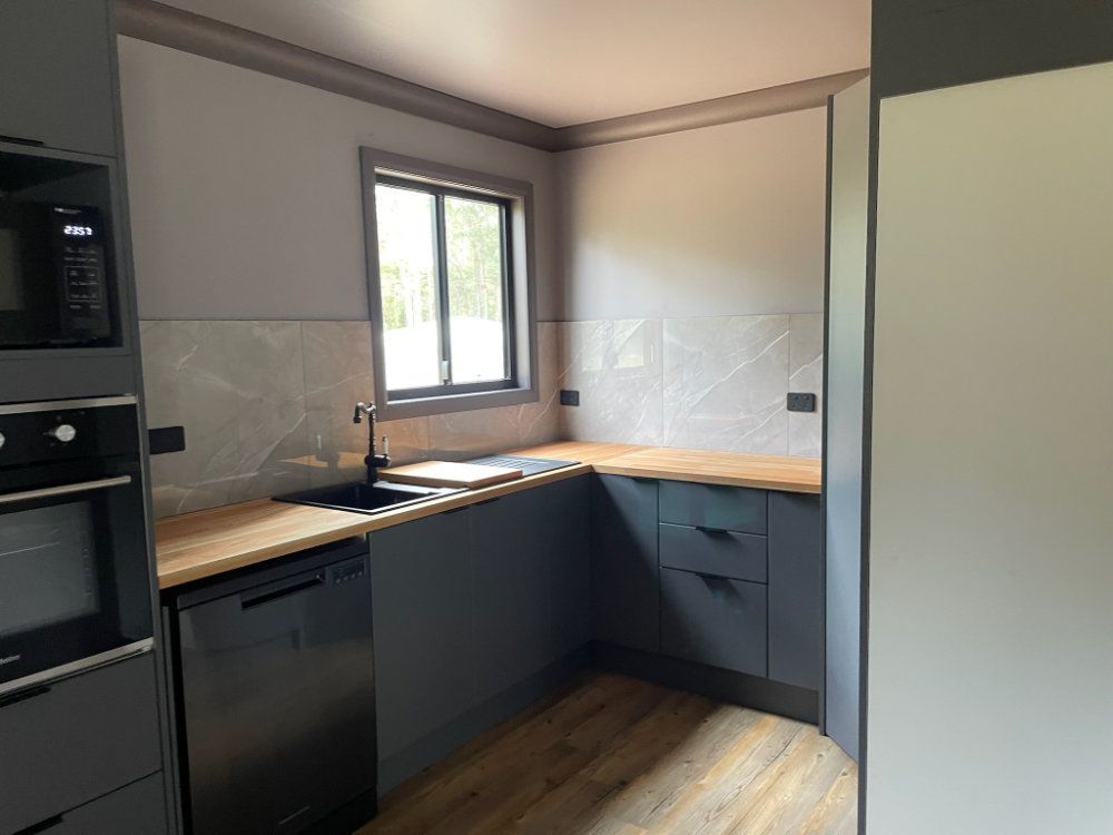 Dark gray kitchen with wood counters, stainless steel appliances, and light gray tiled backsplash — Steel Homes Australia in Branyan, QLD