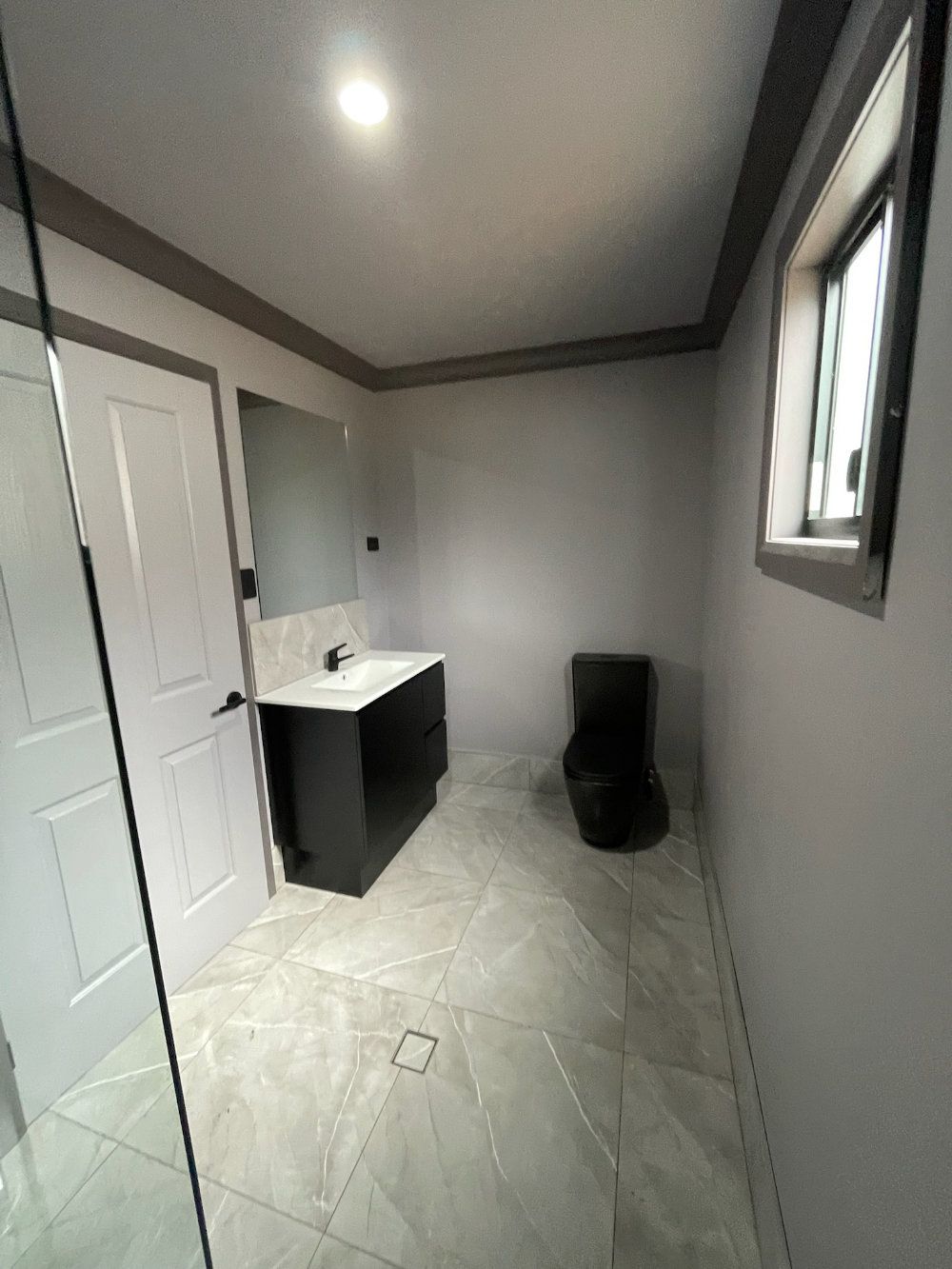 A bathroom with gray walls, black vanity, toilet, and light-colored tile floor — Steel Homes Australia in Branyan, QLD