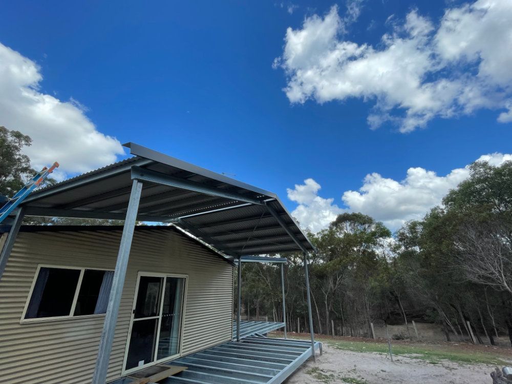 Metal-framed building with a corrugated iron roof under a blue sky with clouds, in a wooded area — Steel Homes Australia in Branyan, QLD