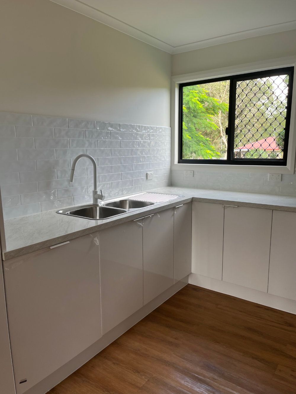 White kitchen with sink, countertops, cabinets, and window — Steel Homes Australia in Branyan, QLD