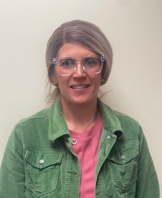 A woman with glasses wearing a green shirt smiles for the camera