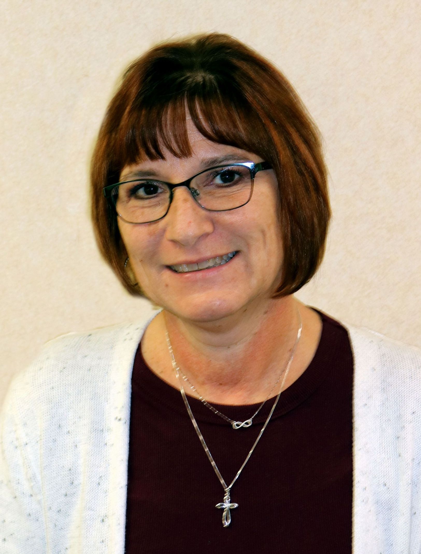 A woman wearing glasses and a cross necklace is smiling for the camera.