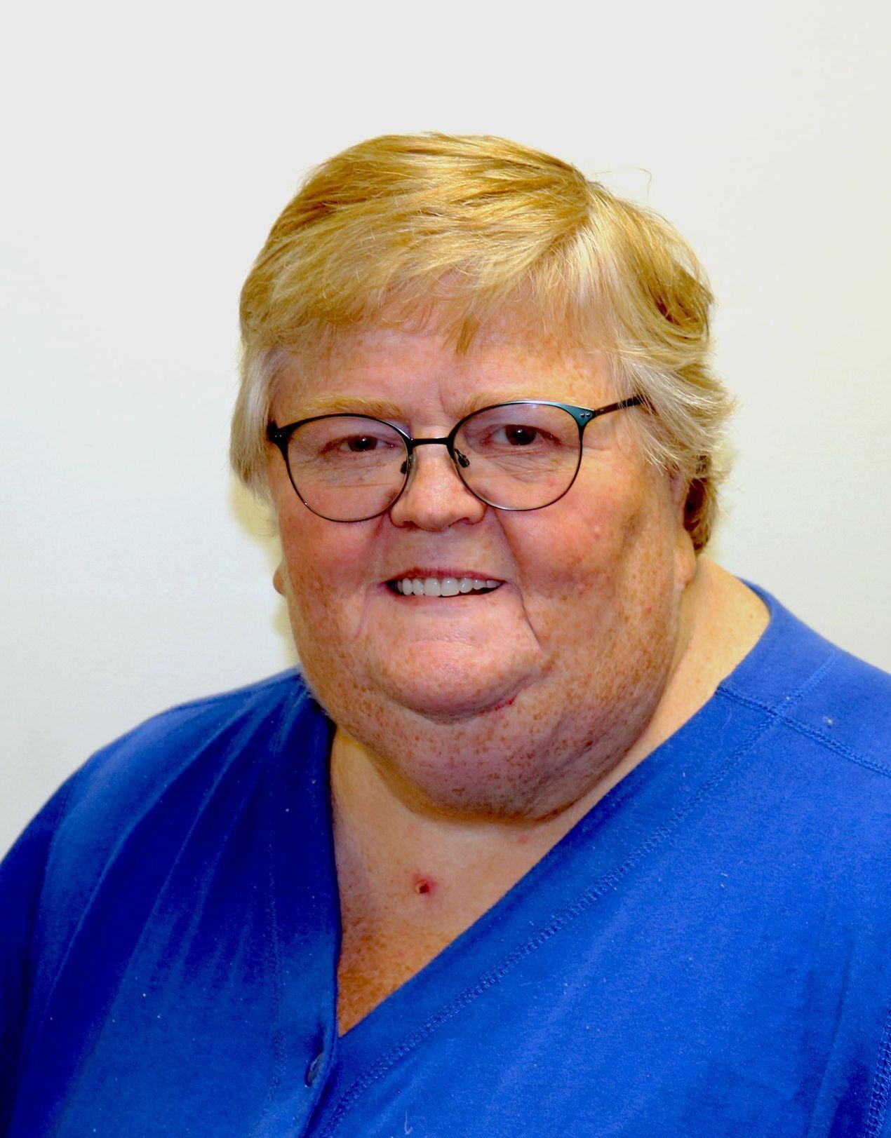 A woman wearing glasses and a blue shirt smiles for the camera