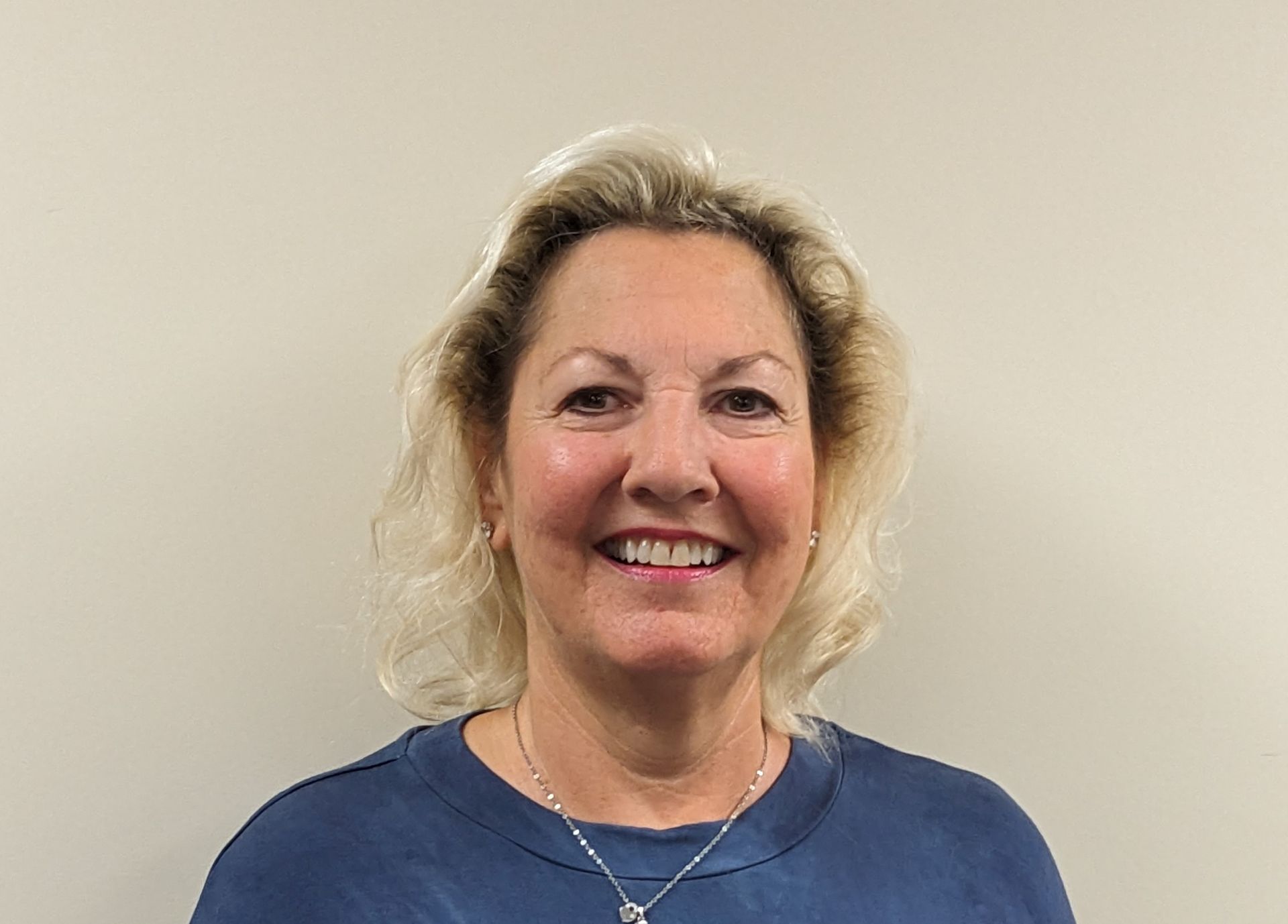 A woman wearing a blue shirt and a necklace is smiling for the camera.