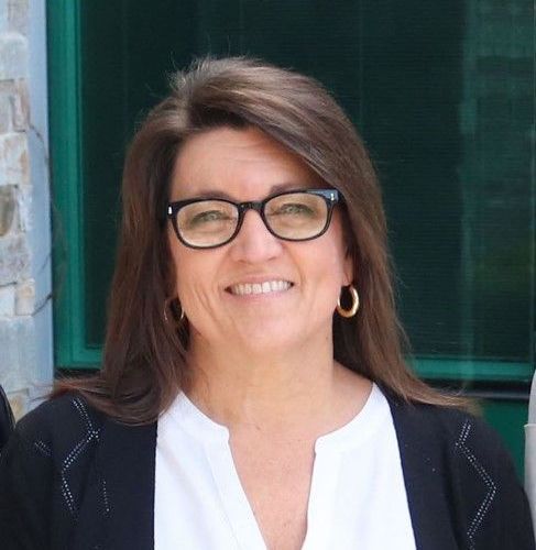 A woman wearing glasses and earrings is smiling for the camera.