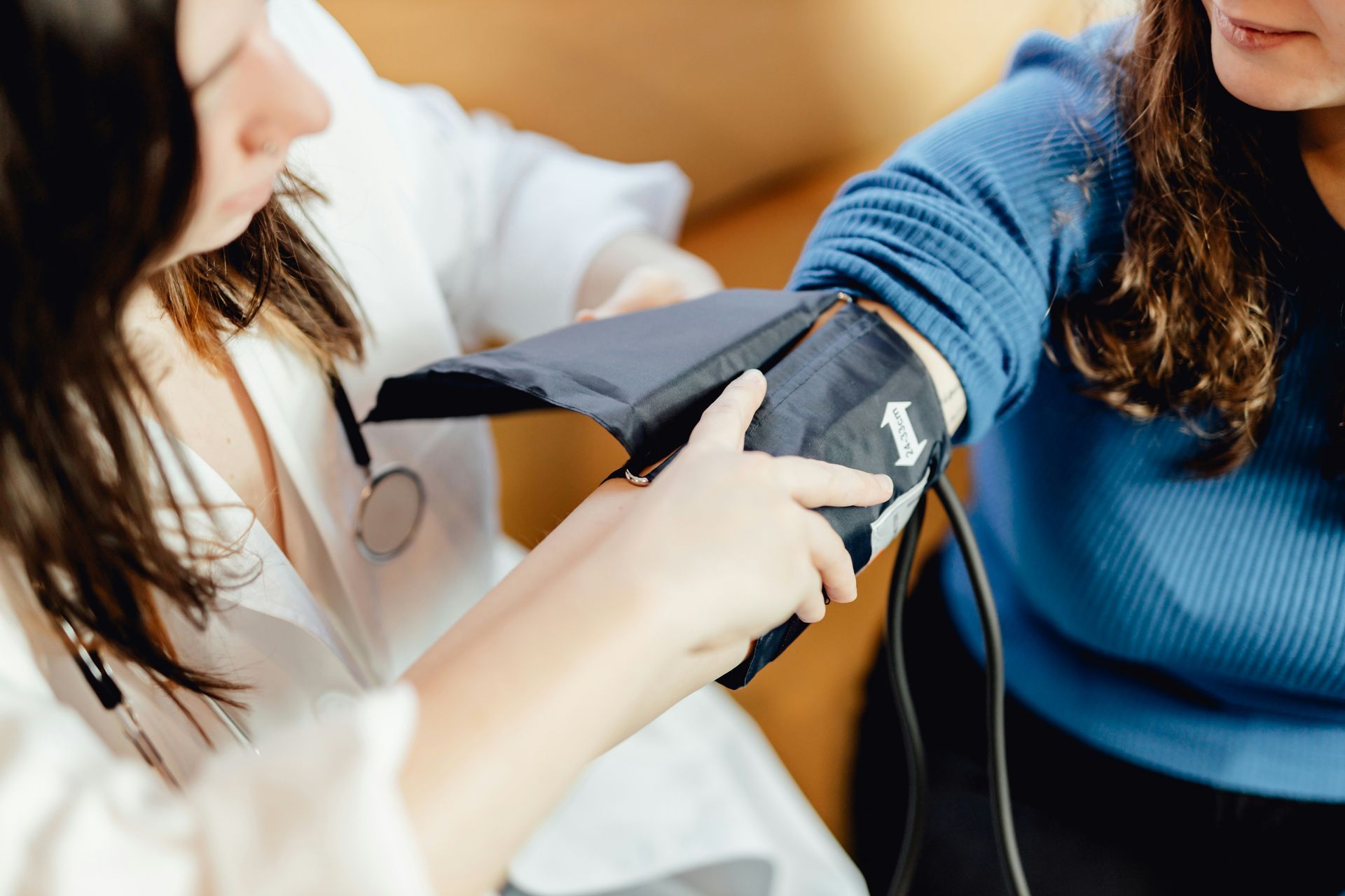 Doctor taking patient's blood pressure with an arm cuff. Indoors, both women visible.