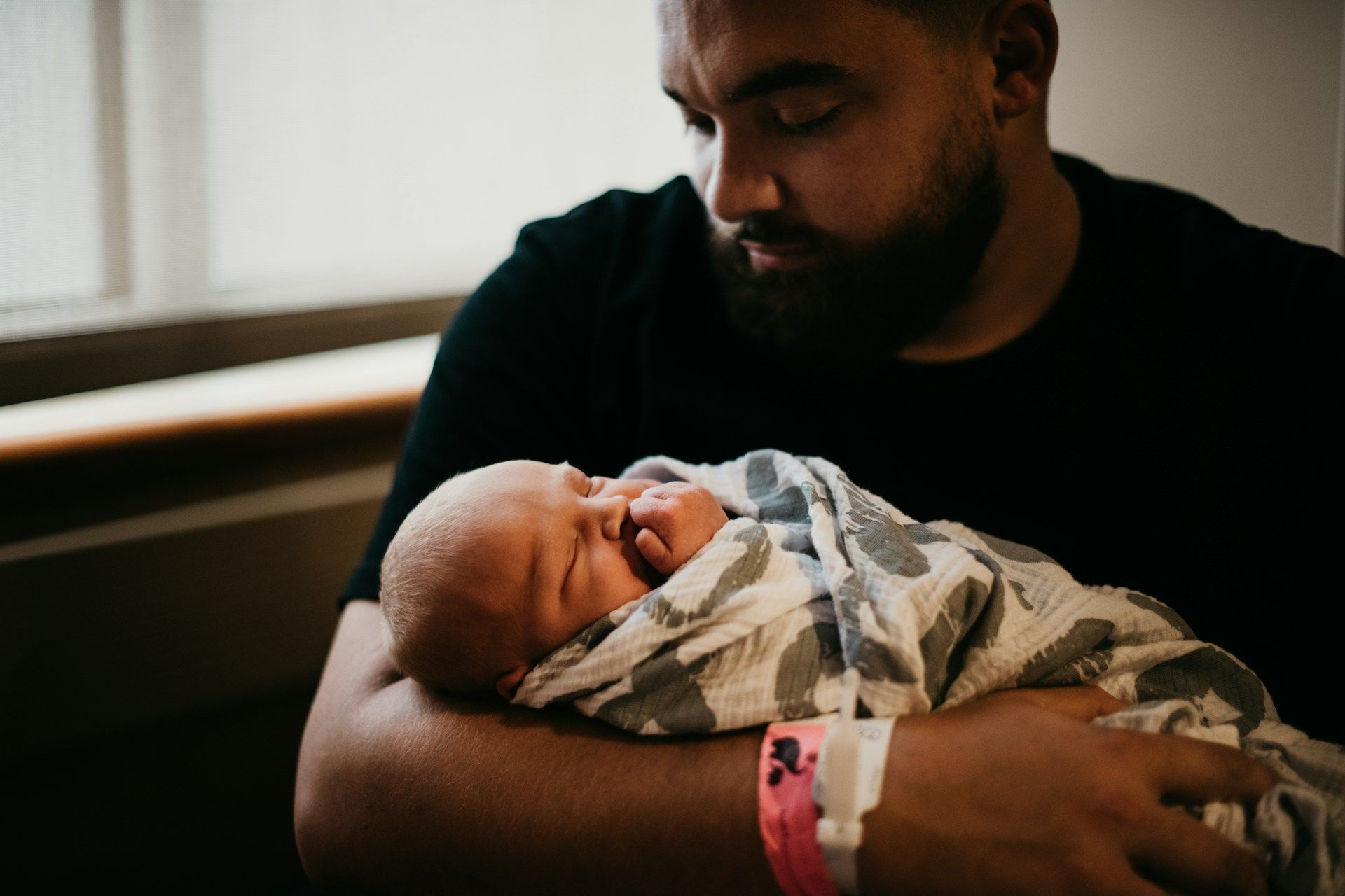 A man is holding a newborn baby wrapped in a blanket in a hospital room.