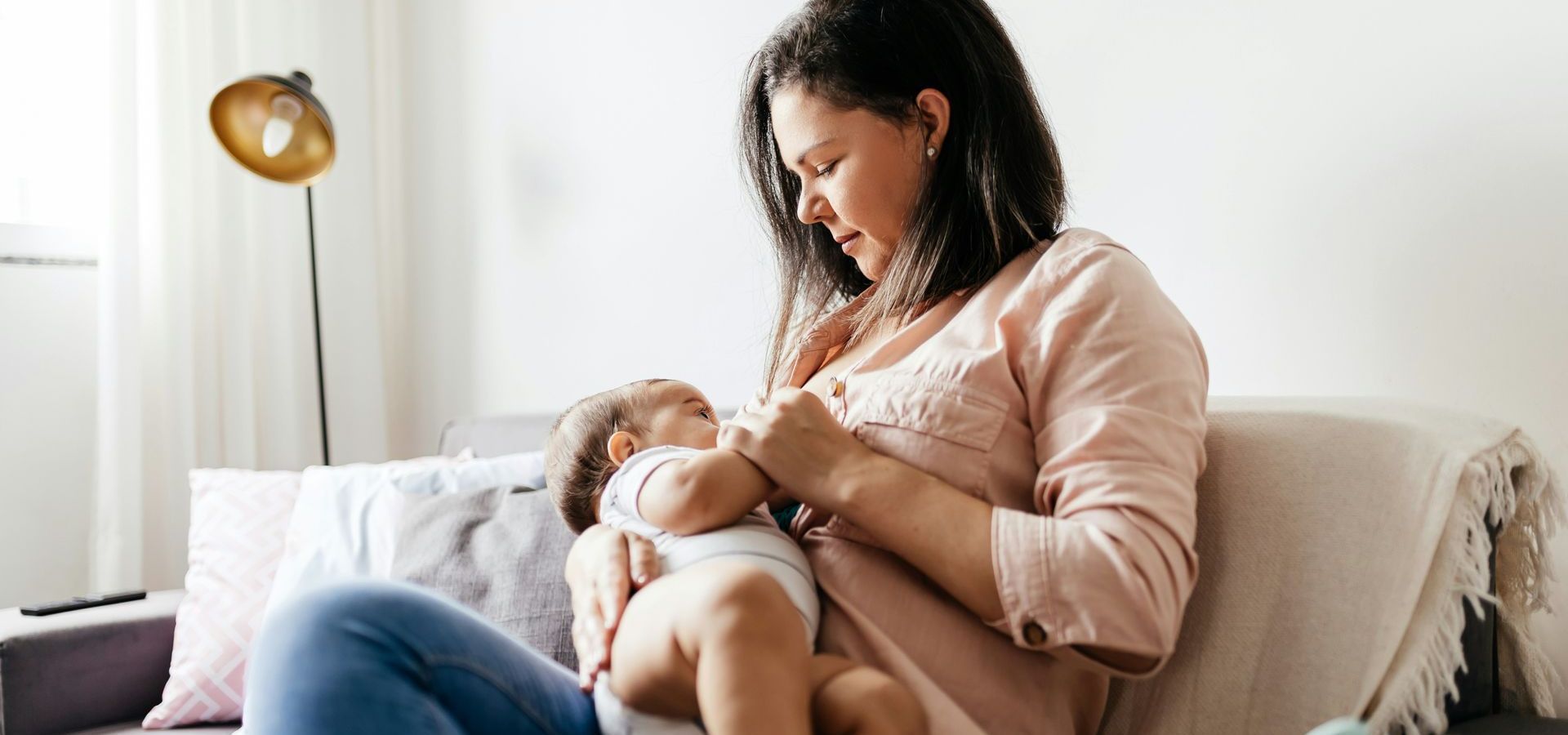 A woman is sitting on a couch breastfeeding her baby.