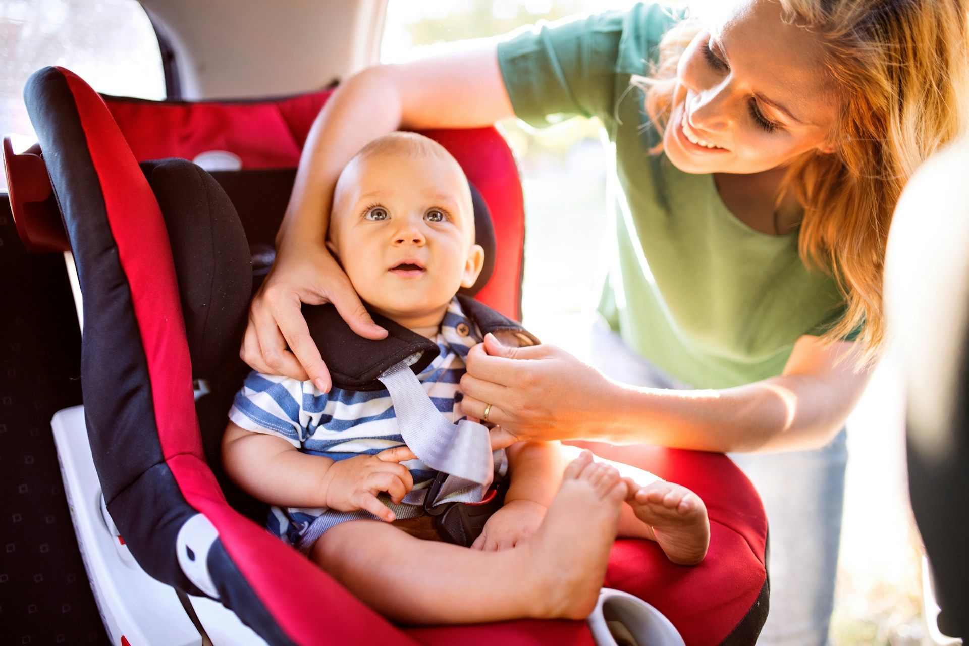 A woman is putting a baby in a car seat.