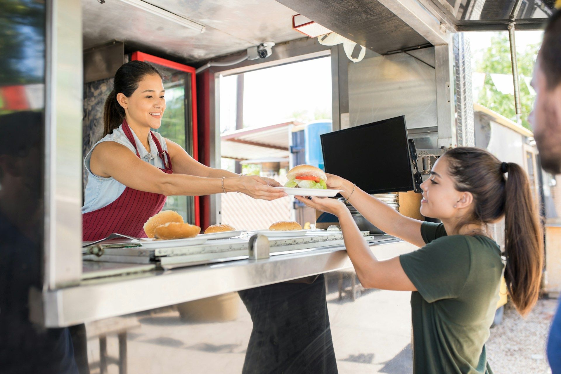 A woman is handing a plate of food to a girl at a food truck.