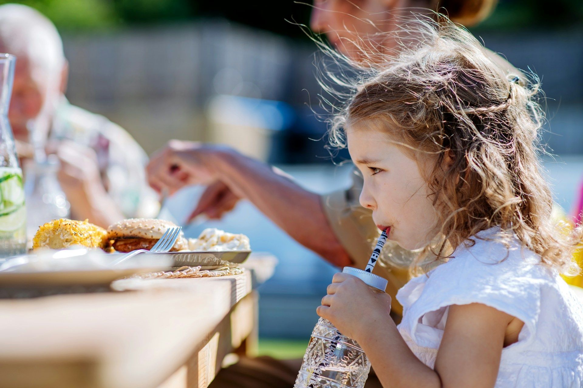 A little girl is drinking water through a straw while sitting at a table.