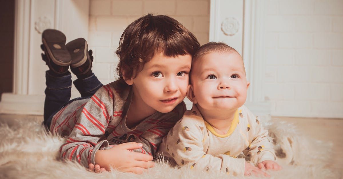 A boy and a baby are laying on the floor together.