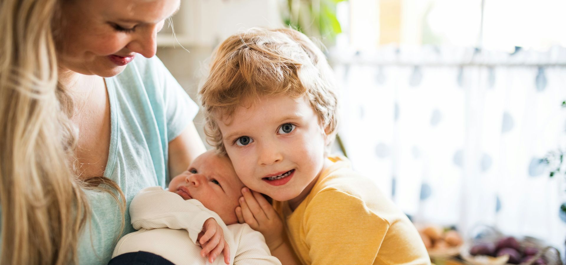 A woman is holding a baby and a little boy.