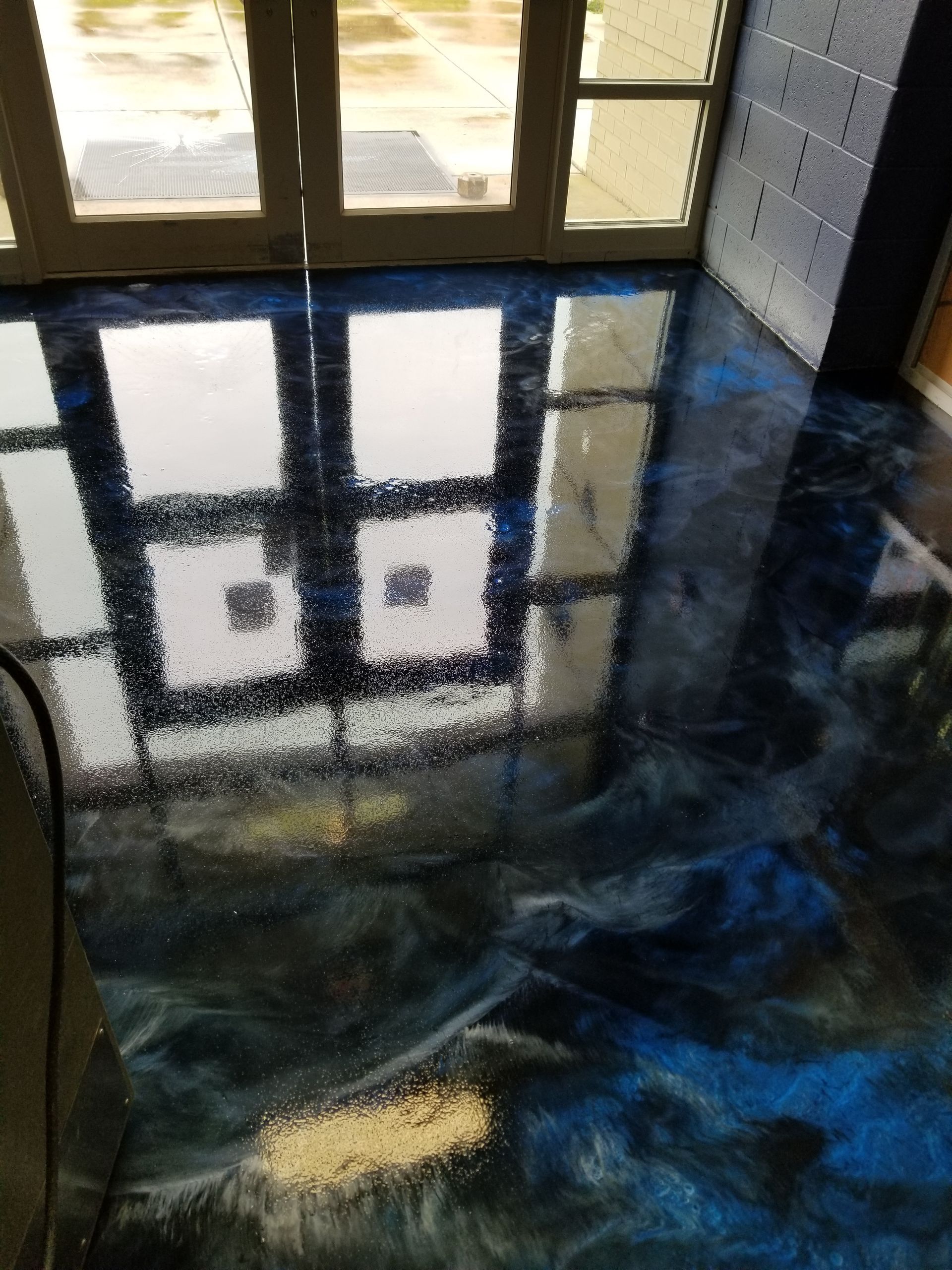 Blue and black epoxy floor with reflective, swirling patterns. Sunlight from a window above is reflected on the floor.