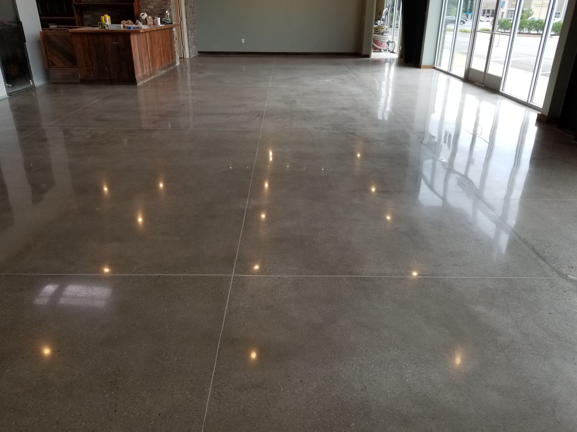 Polished concrete floor in a modern commercial space reflecting light, with a wooden bar and glass doors.