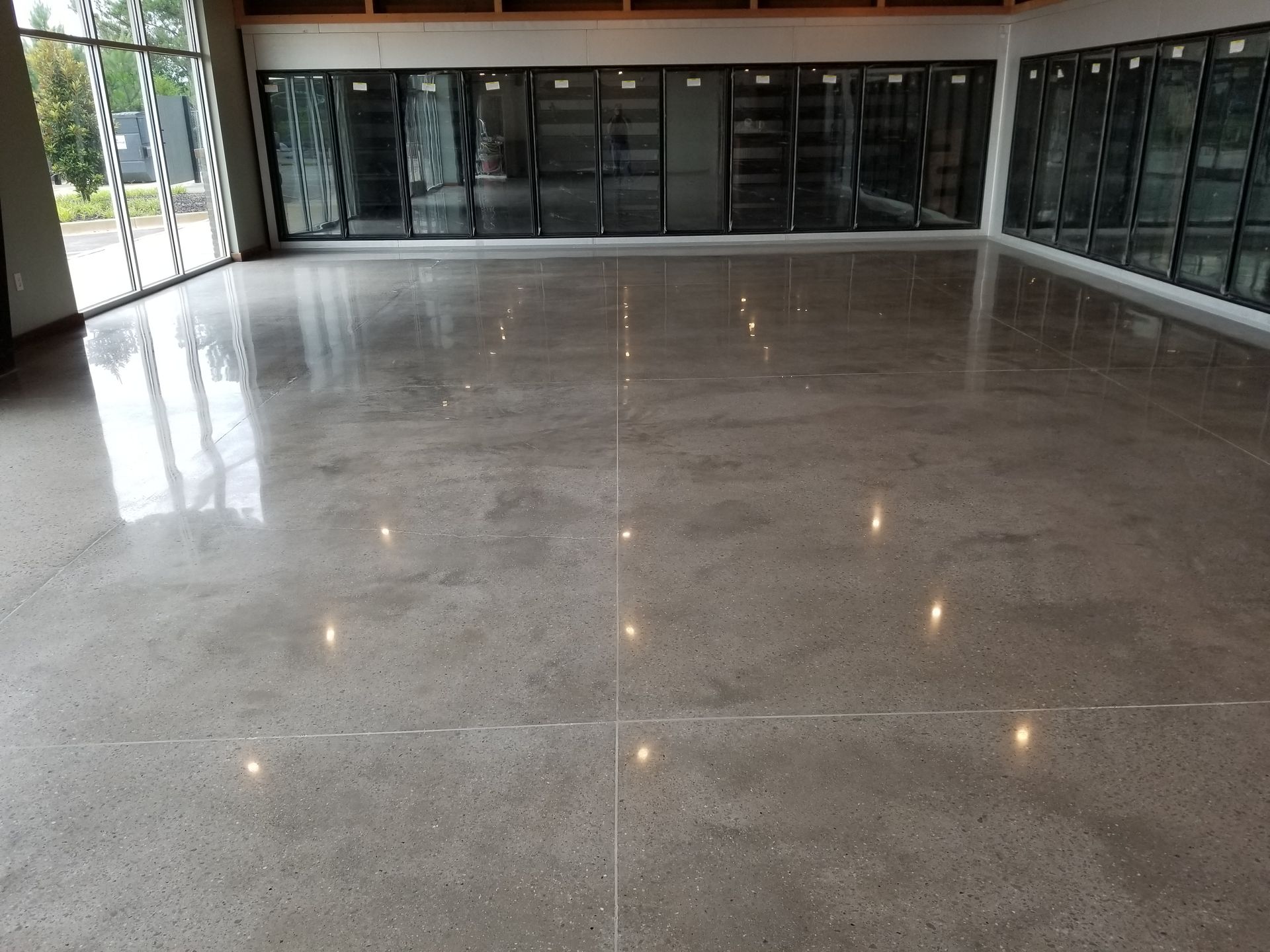 Polished concrete floor reflecting light in a large retail space. Refrigerated display cases line the back wall.