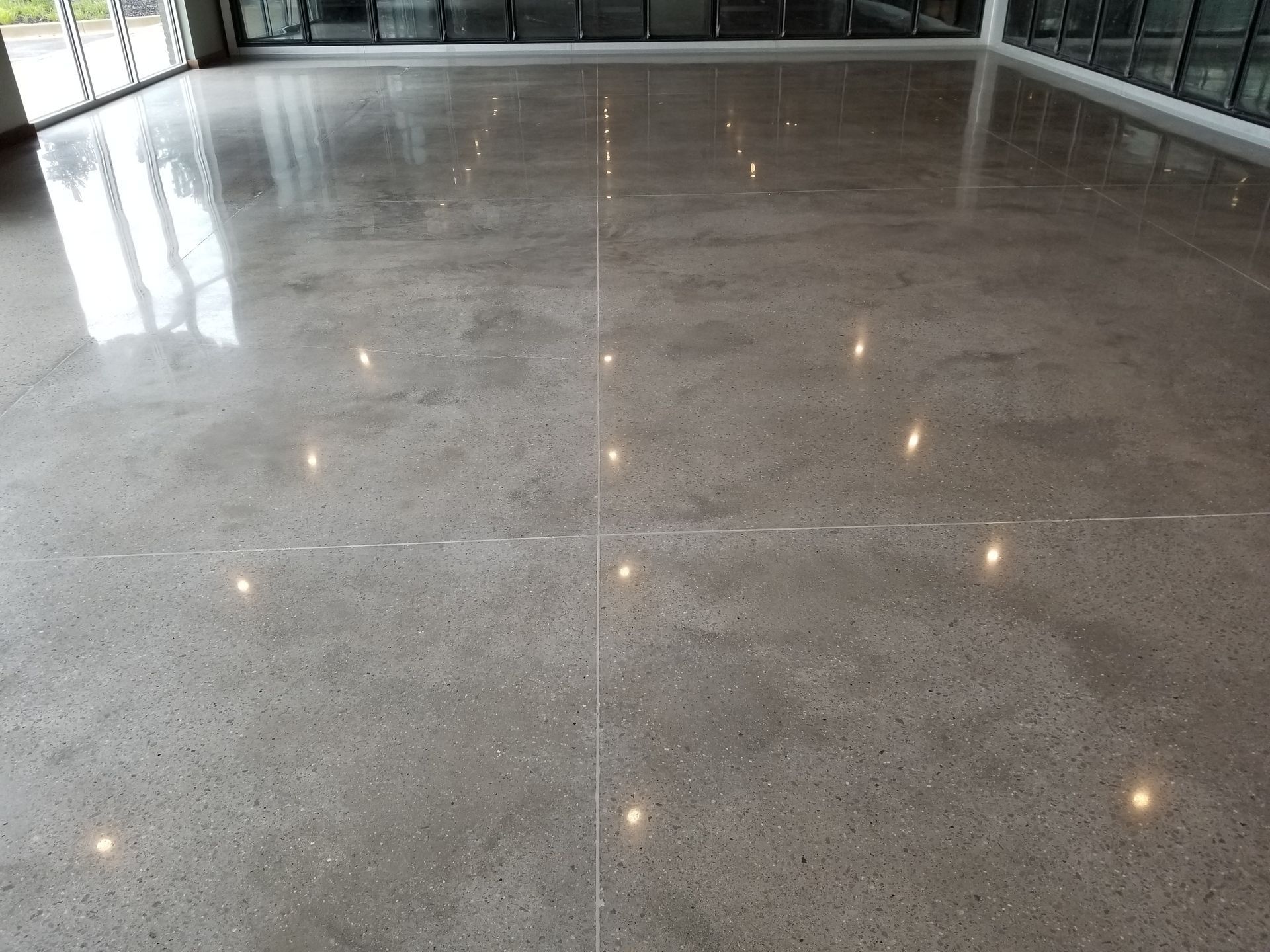 Polished concrete floor reflecting overhead lights in a large open space. The floor is gray with a shiny finish.