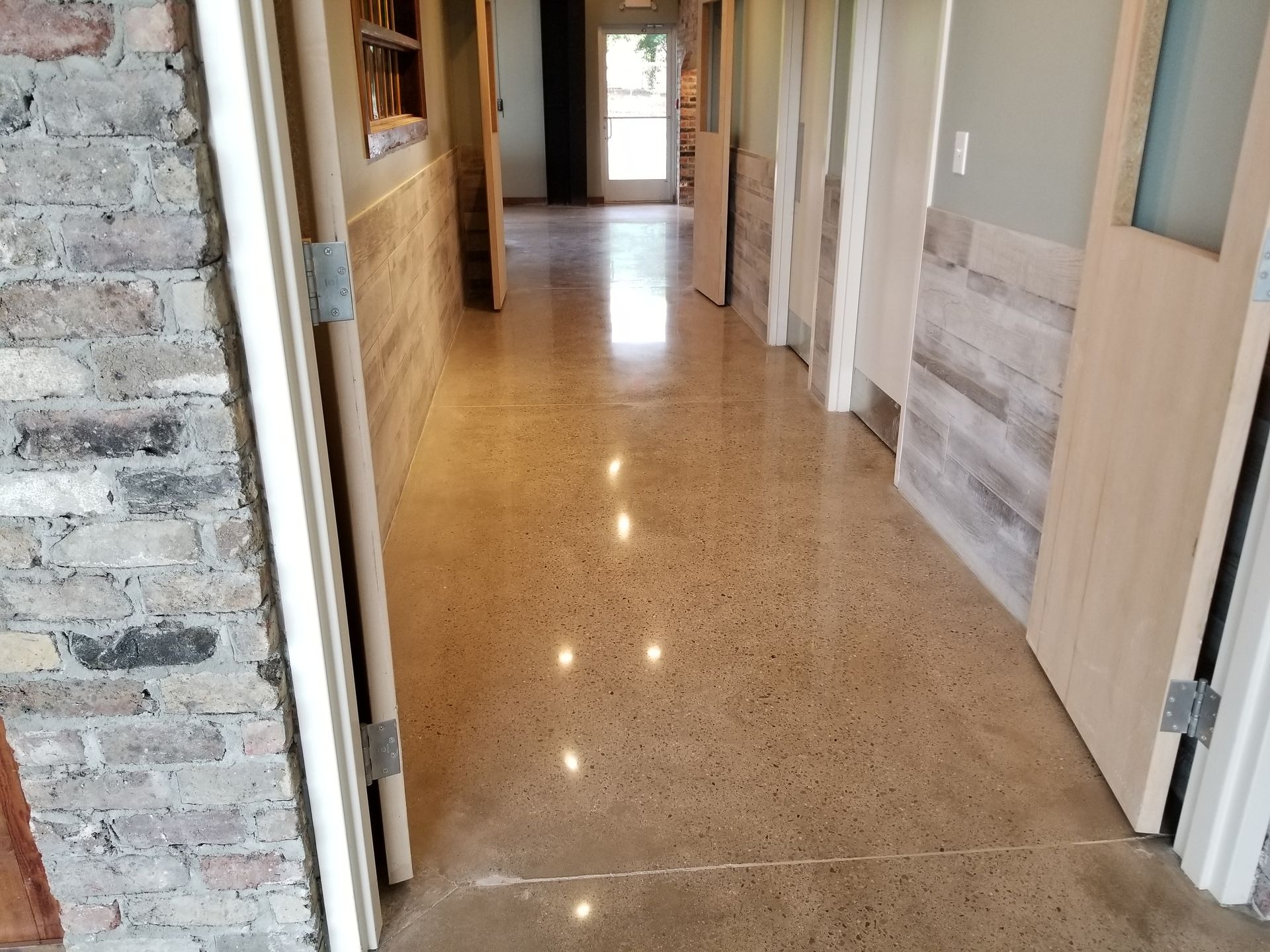 Long hallway with polished concrete floor and wood-paneled walls. Doors line the sides, leading to various rooms.