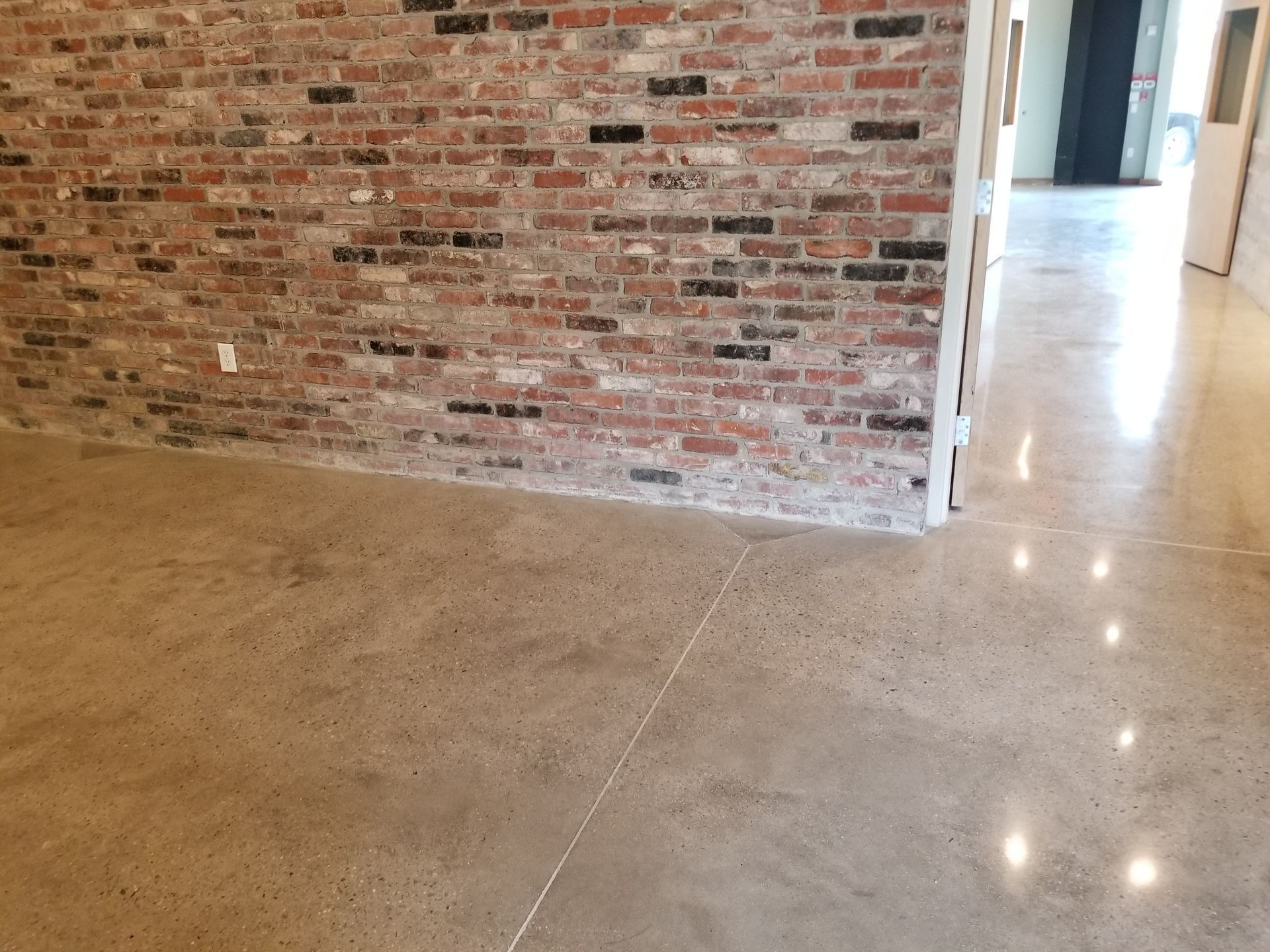 A room with a brick wall and a polished concrete floor. The floor reflects light, creating bright spots.