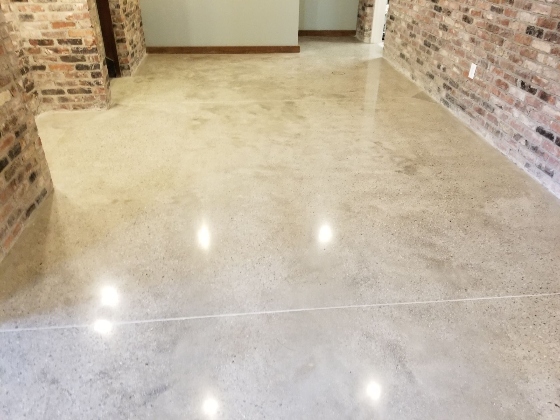 Polished concrete floor reflecting ceiling lights, set in a room with exposed brick walls.