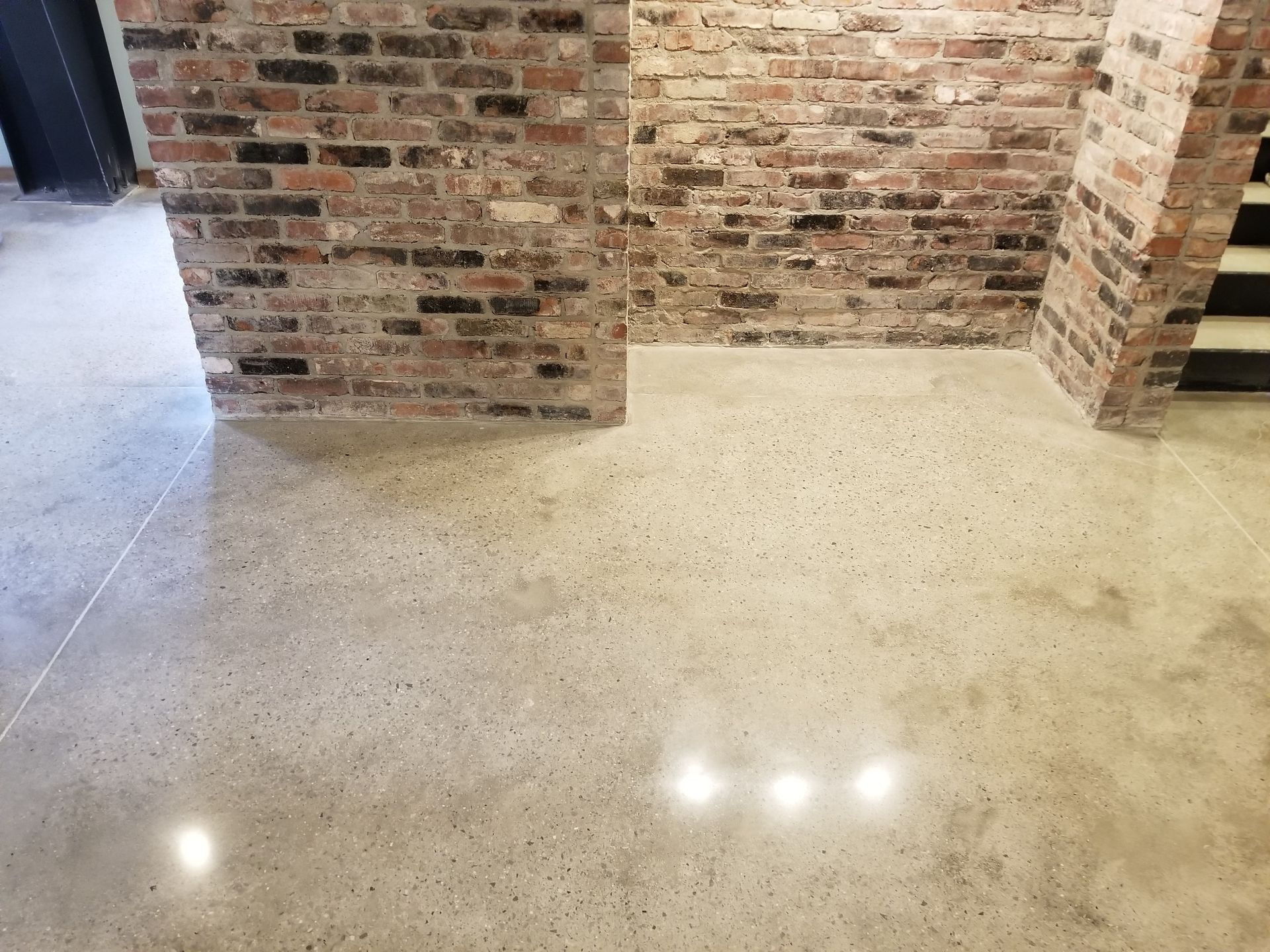 Polished concrete floor with exposed aggregate, framed by brick walls.  Steps lead to an upper level, reflecting light.
