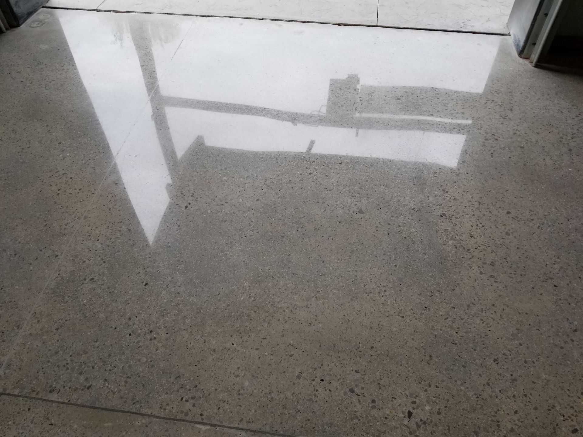 Polished concrete floor reflects light, appearing glossy gray. A doorway frame is visible at the top of the image.
