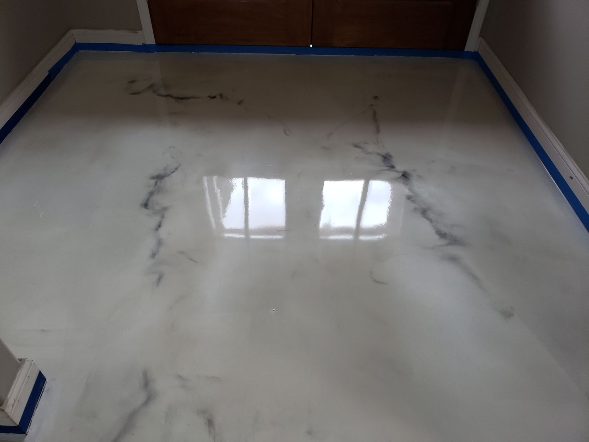 White epoxy flooring with dark swirling patterns, reflecting light from windows. Blue painter's tape lines the edges of the room.