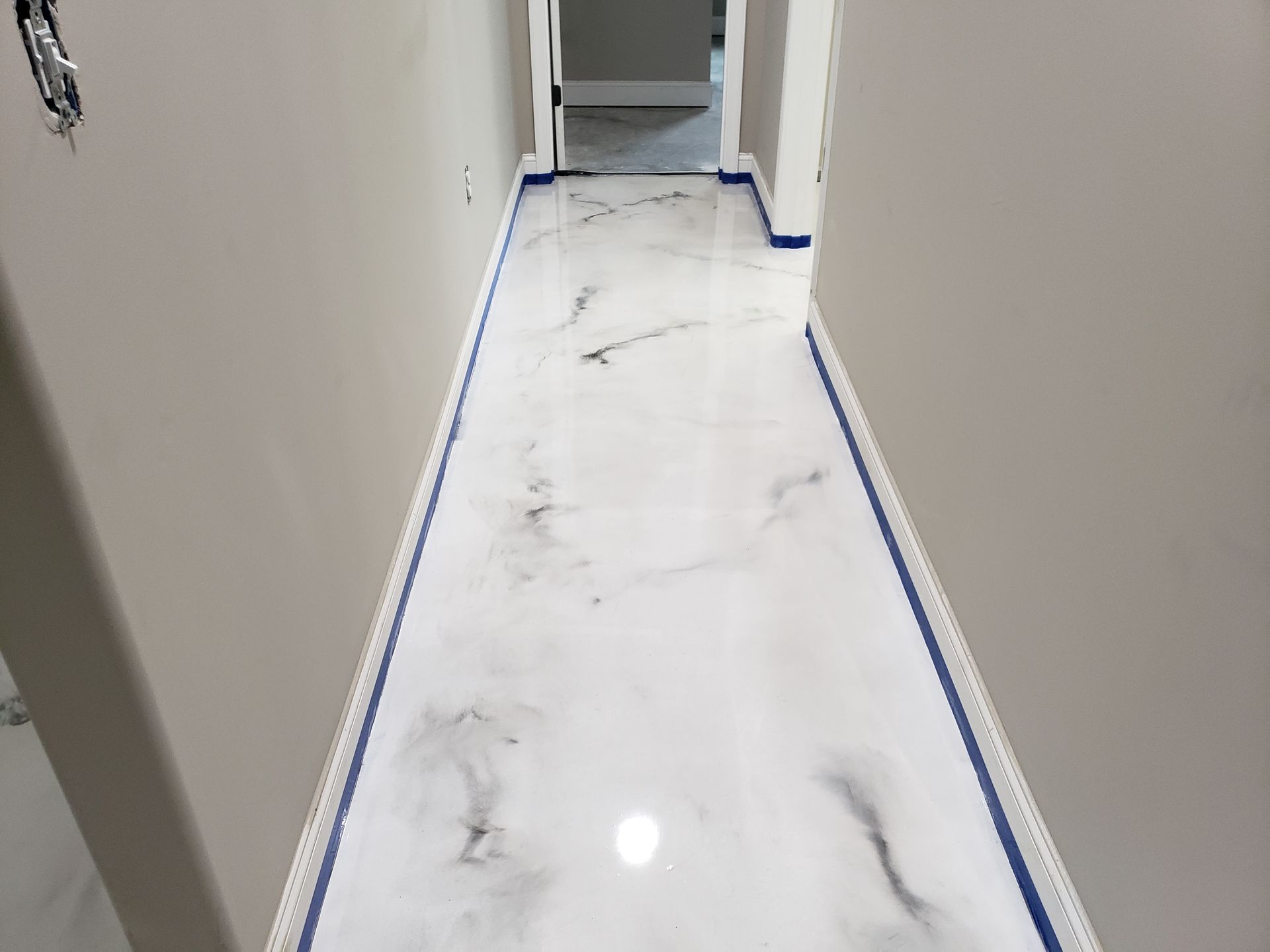 Hallway with white and gray marbled epoxy flooring, blue tape along edges. Gray walls and doorways.