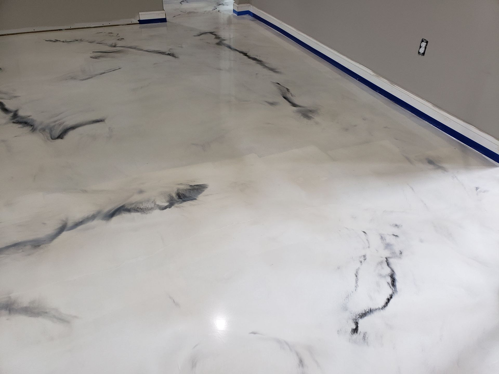 Metallic epoxy floor with white and grey marbled design. Blue tape lines the walls.