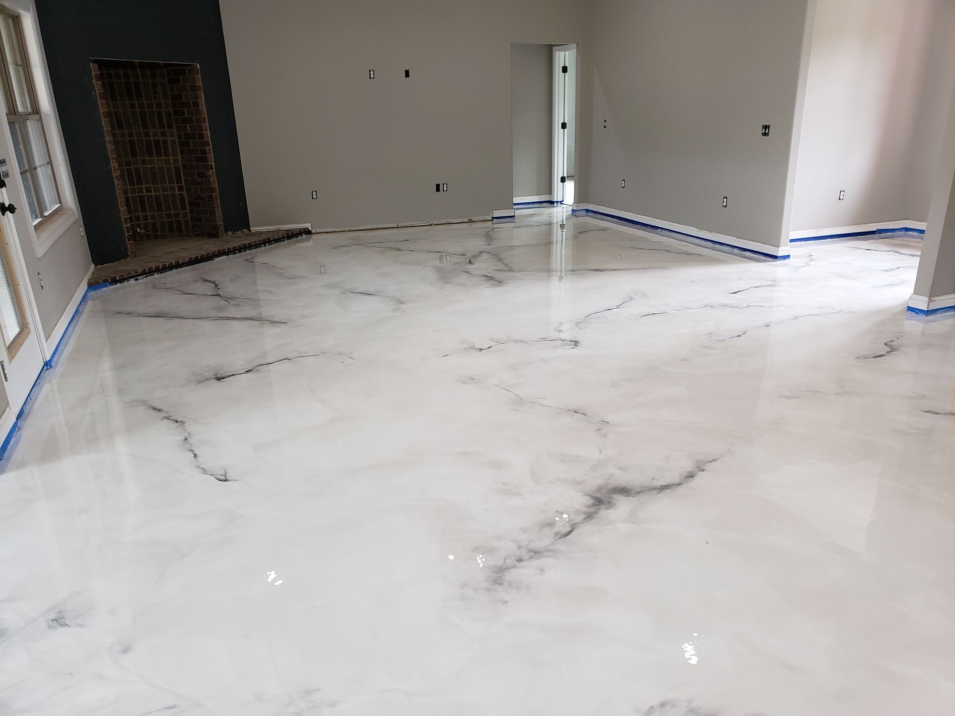 A room with a newly installed, glossy, white and gray marbled epoxy floor, gray walls, and blue painter's tape at the edges.