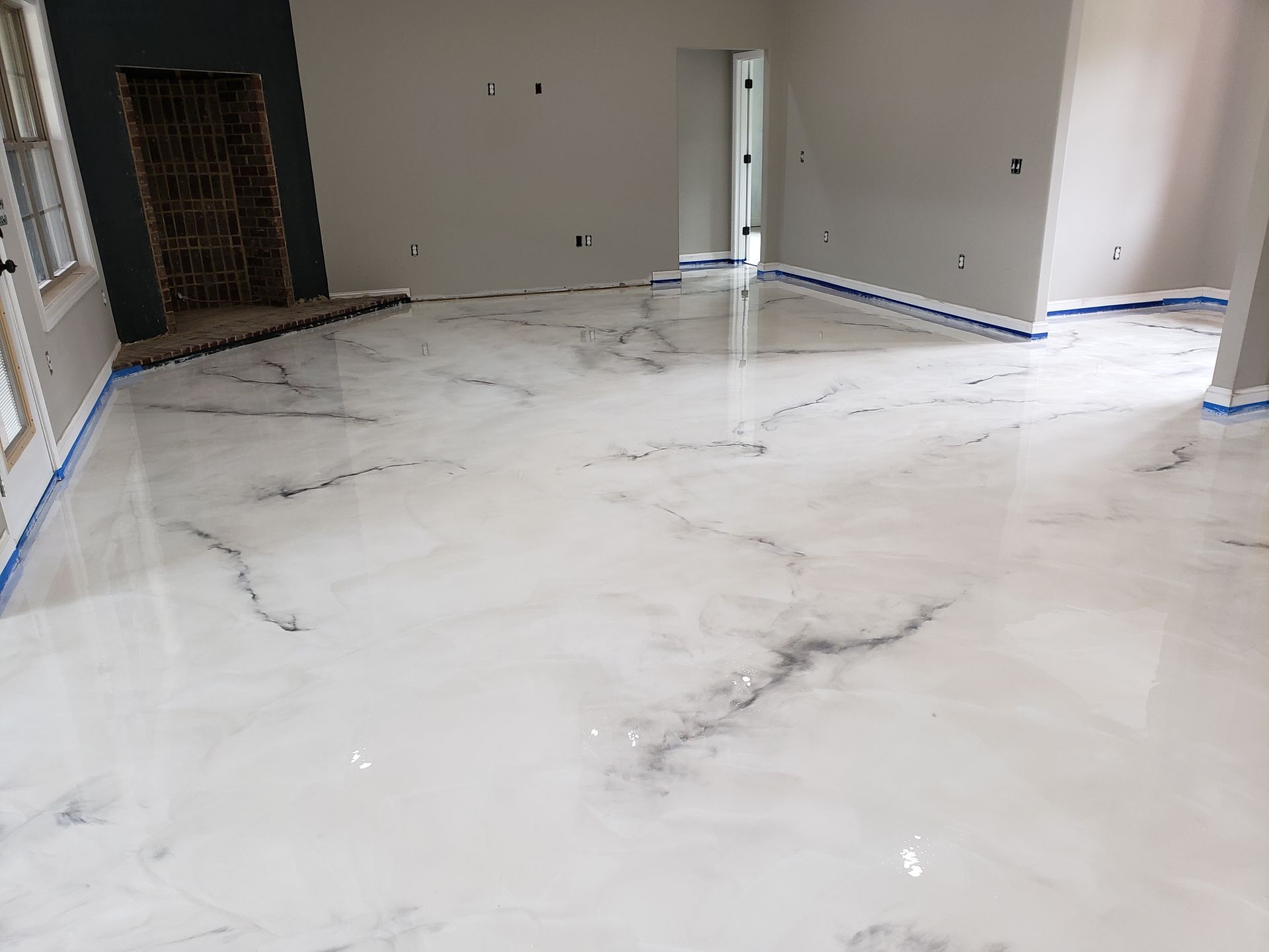 White and gray marble-look epoxy floor in a room, with blue tape along the edges. Gray and white walls and a dark wooden door are visible.