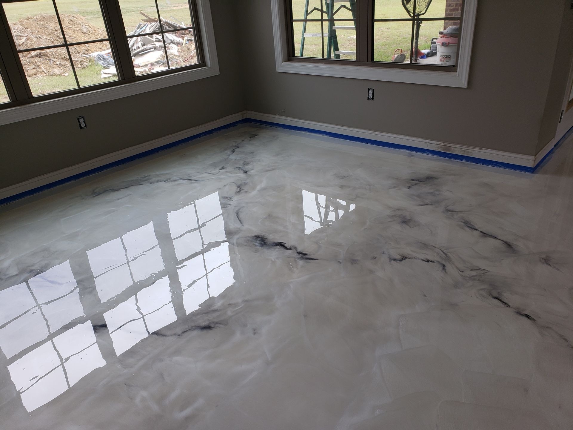 Shiny, white epoxy floor with marble-like veins. Room with windows, blue tape on the baseboards, and light gray walls.