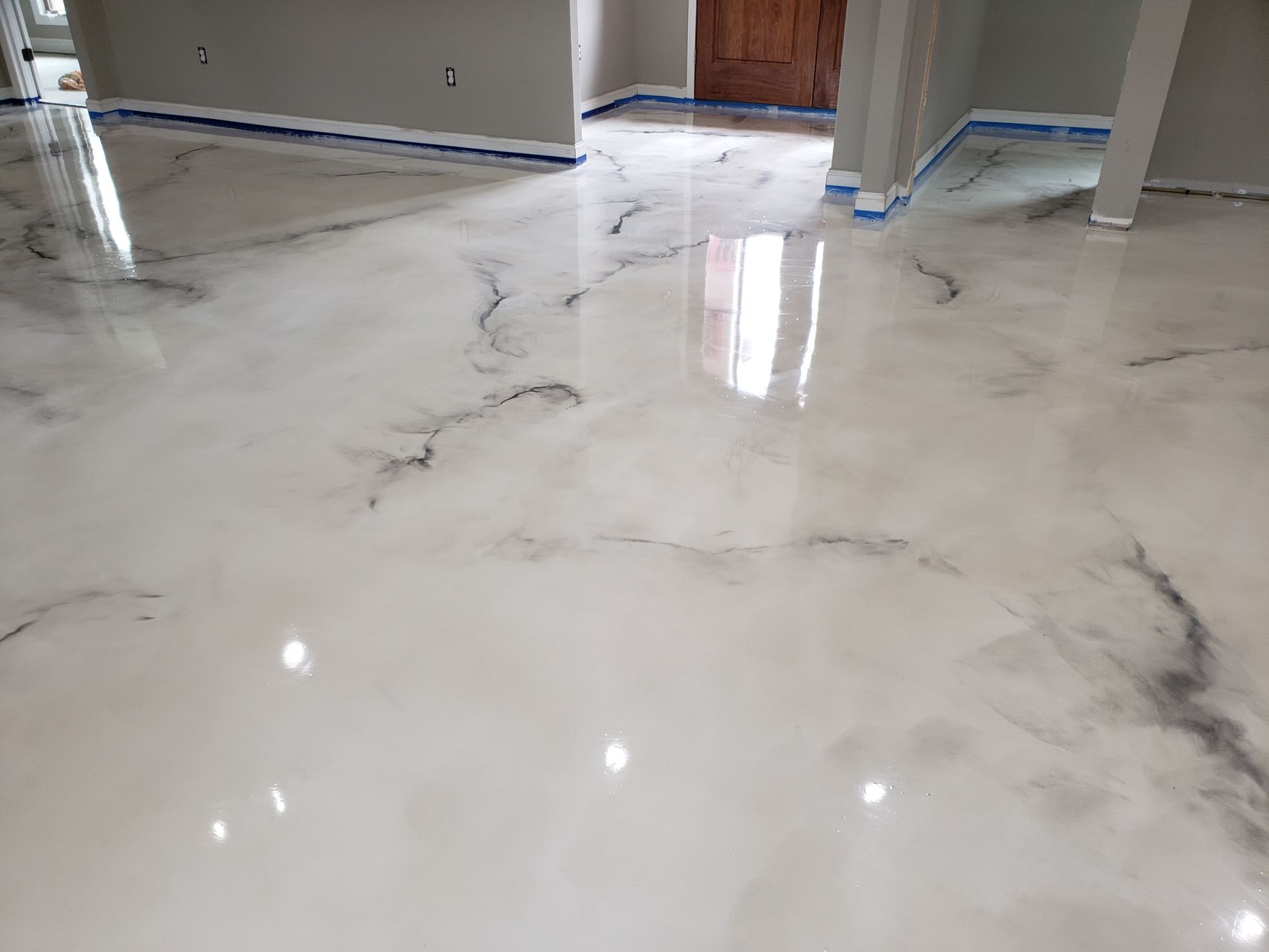Glossy, light-colored epoxy floor with dark veining, reflecting light. The floor appears newly installed in a home.