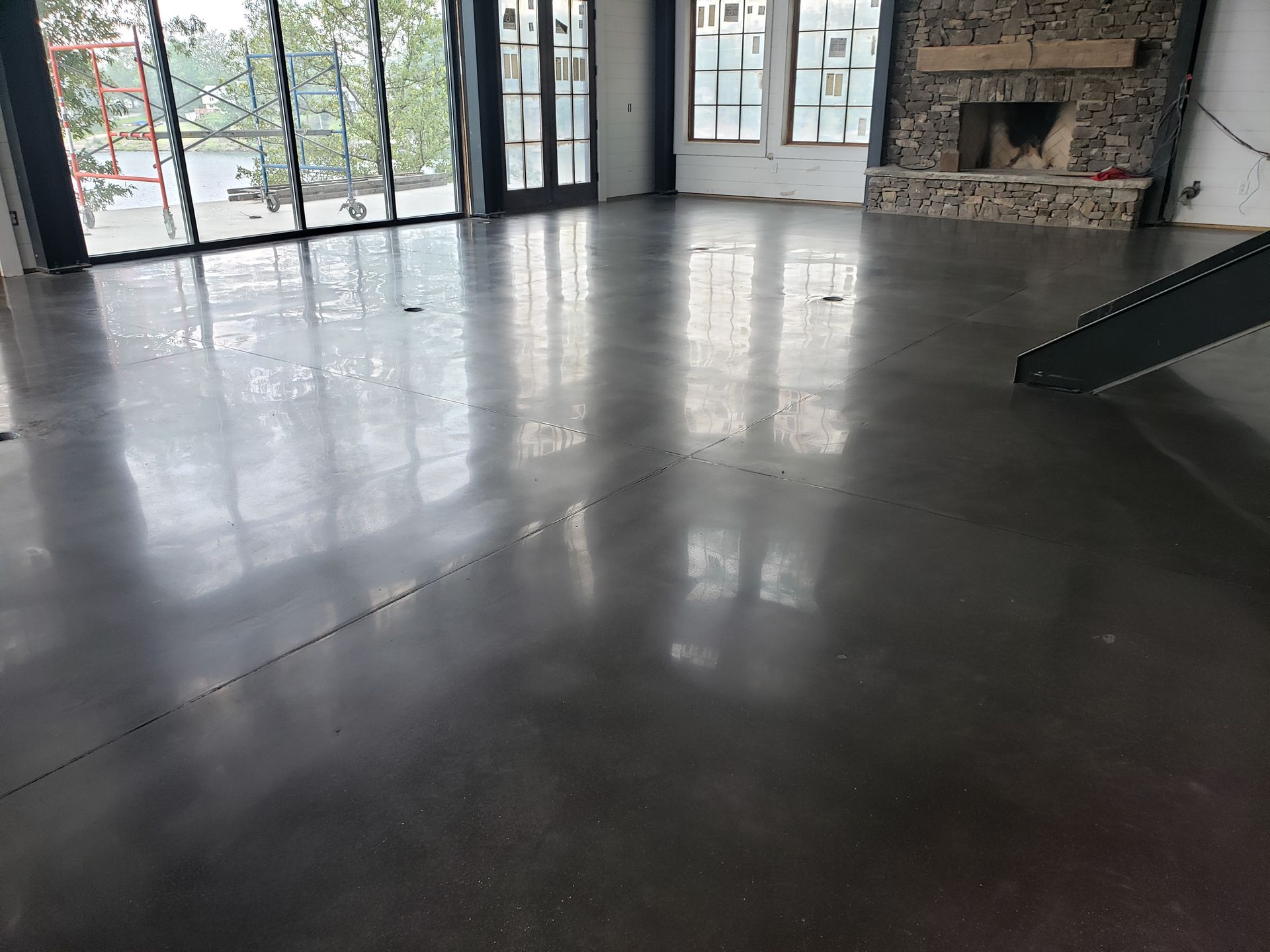 Polished gray concrete floor in a room with large windows and a stone fireplace. The floor reflects light.